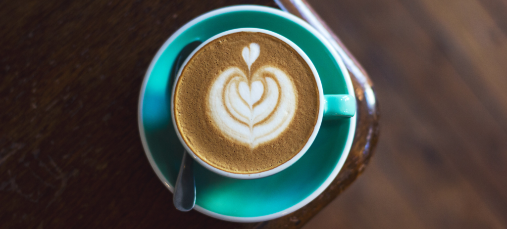 overhead photo of a turquoise coffee cup with hearts made out of latte foam