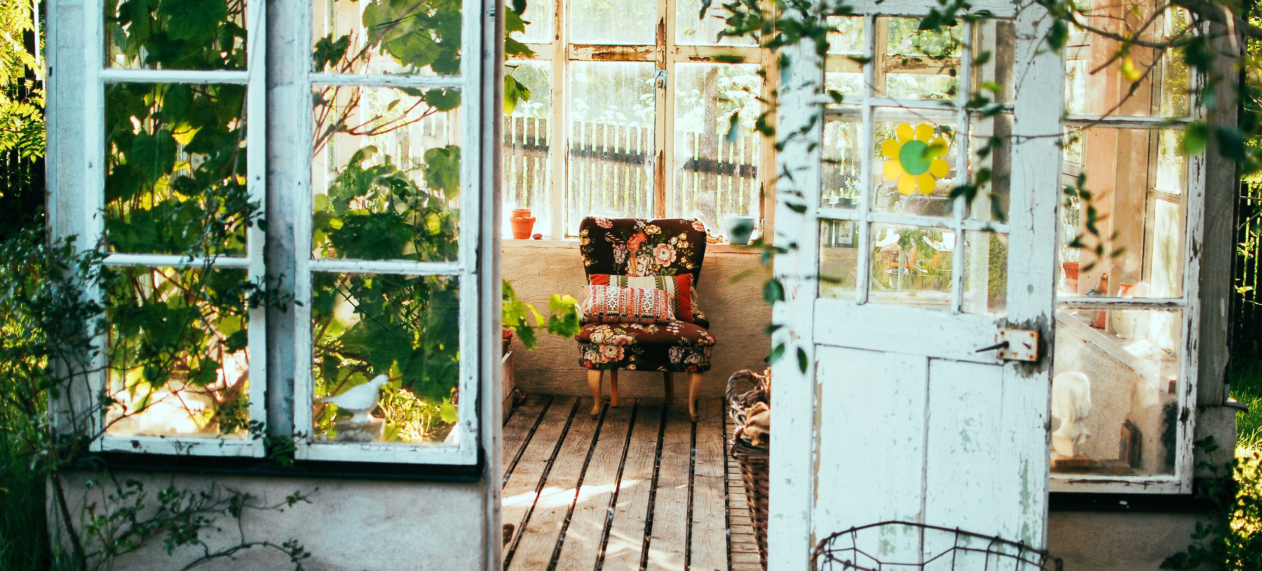 cottage with ivy hanging over white doors and a colorful chair sitting on old wooden floors