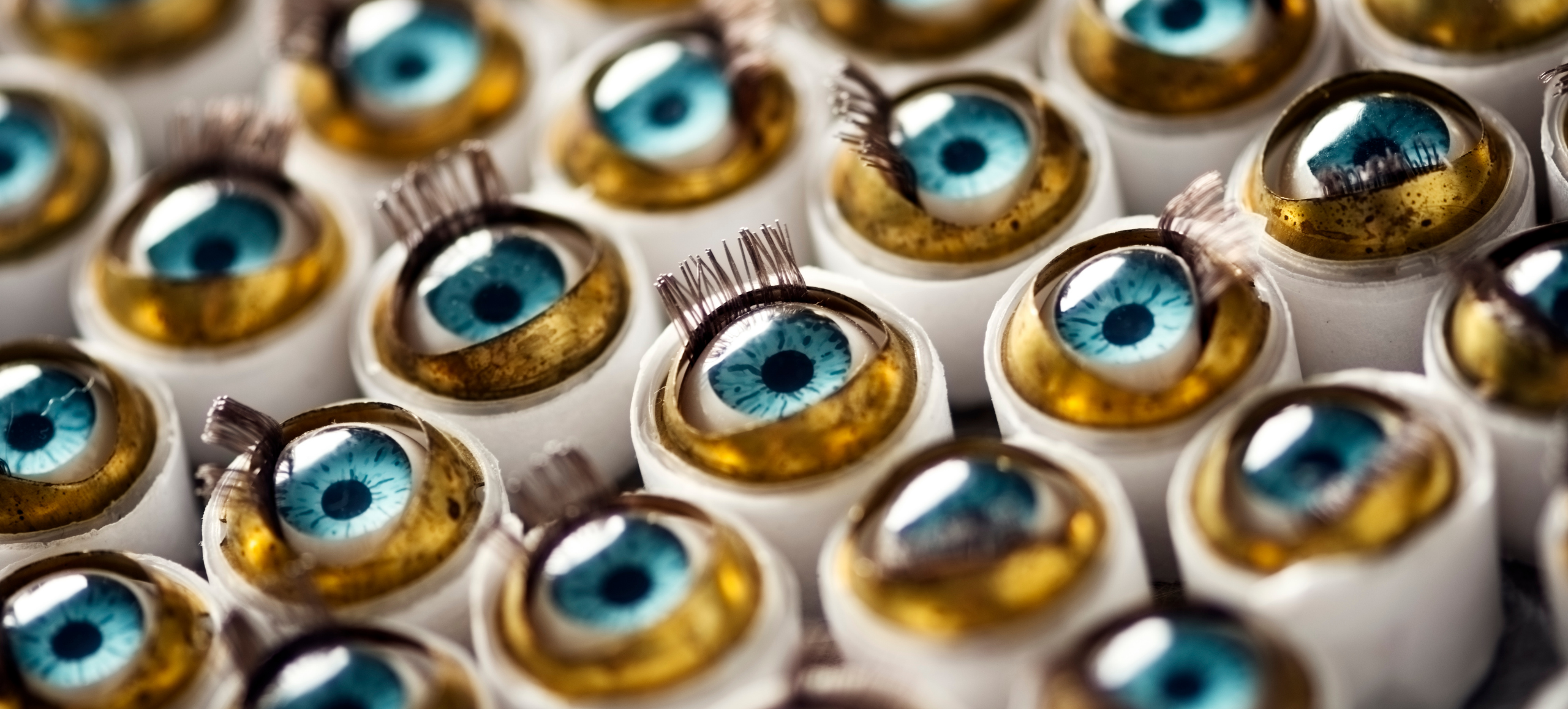 Photo of dozens of blue doll eyes with eyelashes. They each lie in a tiny plastic cup.