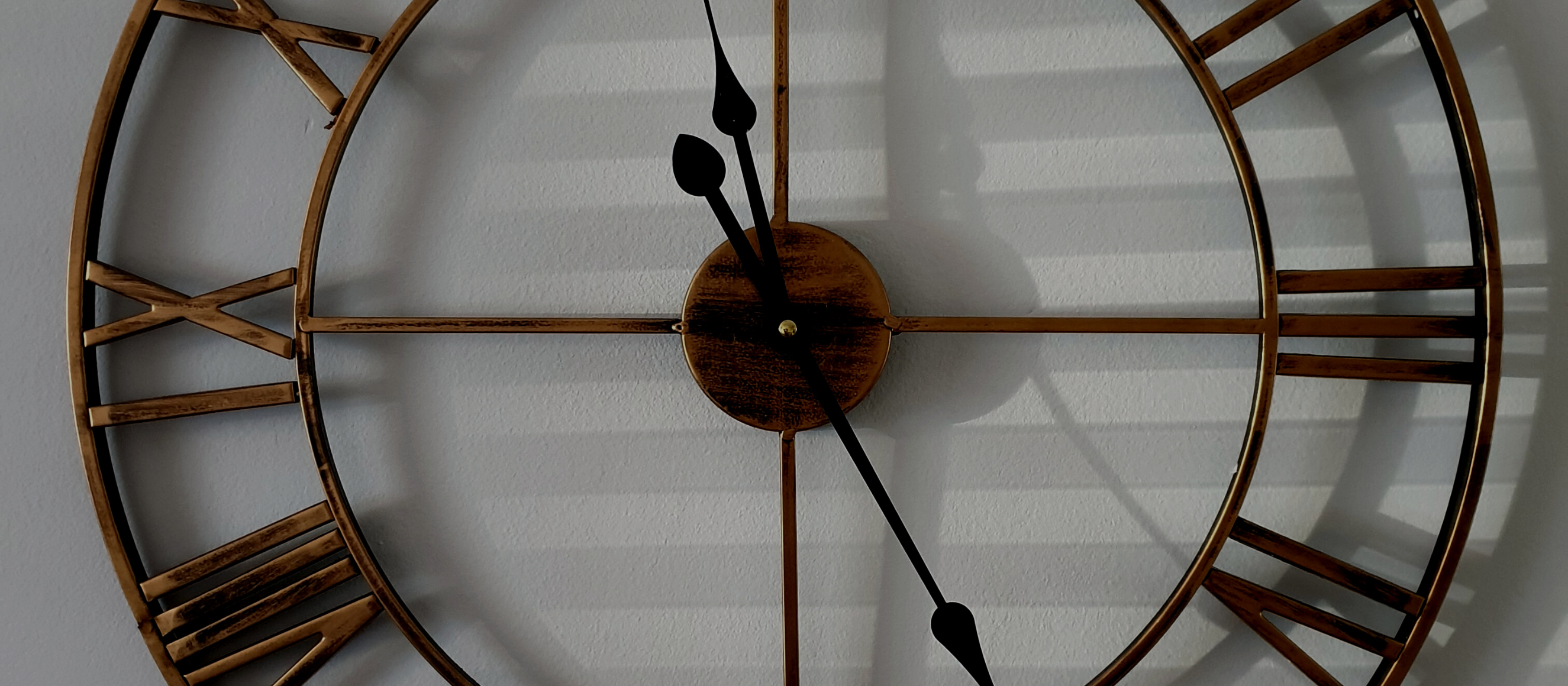 Photo of a large, metal roman numeral clock with shadows cast on the wall behind it