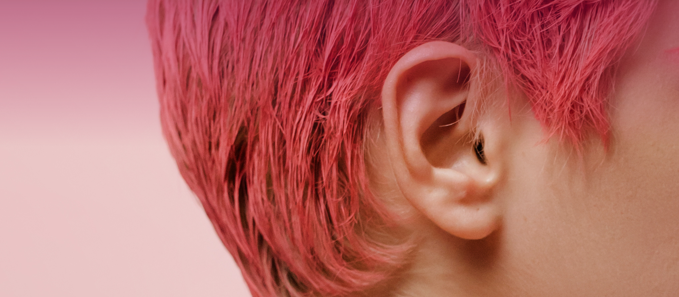 Close-up photo of the side of a woman's head and ear. Her hair is cut into a bright pink pixie cut.